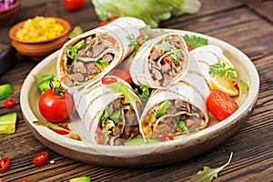 Burritos wraps with beef and vegetables on a wooden background.