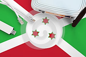 Burundi flag depicted on table with internet rj45 cable, wireless usb wifi adapter and router. Internet connection concept