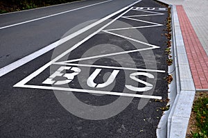 Bus stop consisting of a reserved place with the word bus. Horizontal traffic sign white lines. The concrete curb is rounded due t