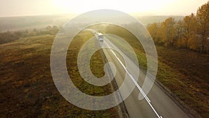 Bus traveling on the asphalt road in a rural autumn landscape at sunset