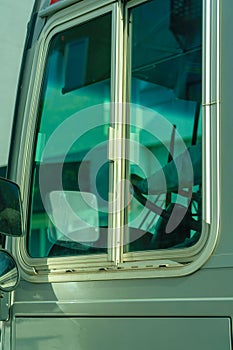 Bus window with blue tint on the glass and gray metal panneling on the side of car
