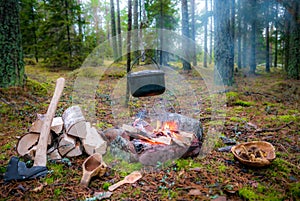 A bushcraft camp fire with hanging pot, axe and kuksa.