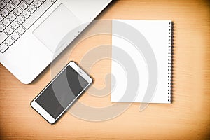Busiiness notebook computer and notebook paper message with smart phone on wooden desk background with film effect
