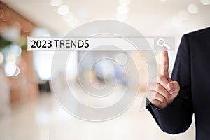 Businesman hand touching 2023 trends search bar over blur office background, banner, SEO 2023 business trends planning, success in