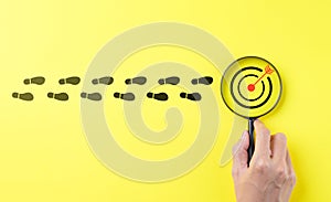 Business achievement goal and objective target concept. Hand holding magnifying glass focusing on target goal on yellow background