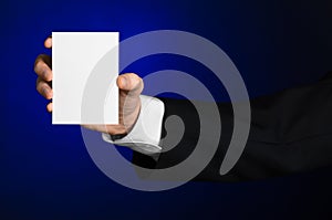 Business and advertising topic: Man in black suit holding a white blank card in his hand on a dark blue background in studio