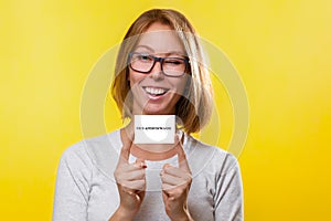 Business and advertising. The young woman the blonde in glasses, holds index fingers both hands Bank card or business card. Yellow