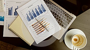 Business analysis on graphs, financial companies and office use, calculator with laptop paper and coffee mugs on the table.