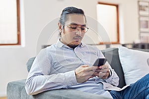 The business app that helps him stay on track. a young businessman using a smartphone on a sofa in a modern office.