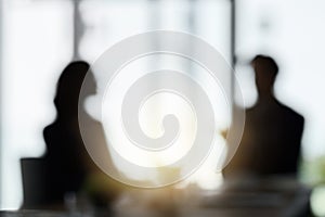 Business as usual. Defocussed shot of two silhouetted businesspeople having a meeting in the boardroom.