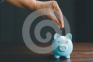 Business asian woman hand put coins in piggy bank on wood table background, saving money wealth and financial concept, finance,