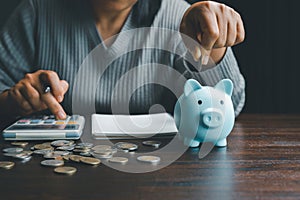 Business asian woman hand put coins in piggy bank on wood table background, saving money wealth and financial concept, finance,
