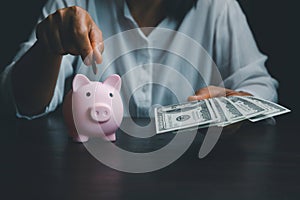 Business asian woman hand put coins in piggy bank on wood table background, saving money wealth and financial concept, finance,