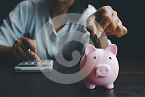 Business asian woman hand put coins in piggy bank on wood table background, saving money wealth and financial concept, finance,