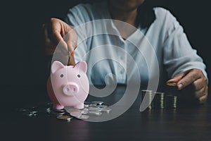 Business asian woman hand put coins in piggy bank on wood table background, saving money wealth and financial concept, finance,