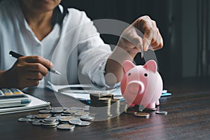 Business asian woman hand put coins in piggy bank on wood table background, saving money wealth and financial concept, finance,