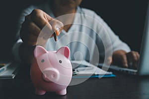 Business asian woman hand put coins in piggy bank on wood table background, saving money wealth and financial concept, finance,