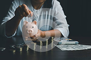 Business asian woman hand put coins in piggy bank on wood table background, saving money wealth and financial concept, finance,