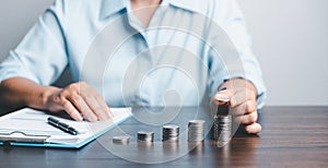 Business asian woman hand put coins in piggy bank on wood table background, saving money wealth and financial concept, finance,