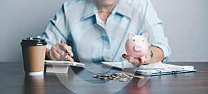 Business asian woman hand put coins in piggy bank on wood table background, saving money wealth and financial concept, finance,