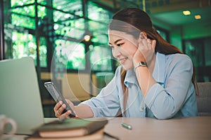 Business asian woman sitting at her desk with laptop using mobile phone during checking an email or social media on internet