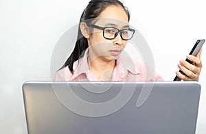 Business Asian young woman holding mobile phone while eyes looking at laptop. Using multiple devices on a desk at home