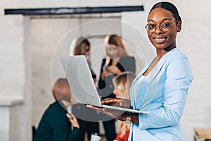 Business black woman adjusting laptop, standing with office colleagues behind