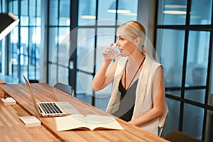 Business blonde girl drinking water in front of a laptop