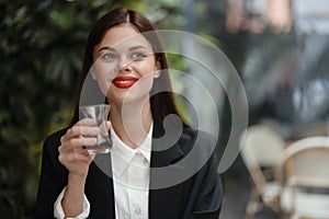 Business brunette woman with red lips smile with teeth drinks tea in a cafe from a Turkish glass mug in a white shirt