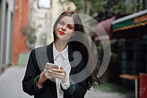 Business brunette woman with red lips smile with teeth with a phone in her hands, white shirt and black jacket fashion