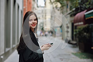 Business brunette woman with red lips smile with teeth with a phone in her hands, white shirt and black jacket fashion
