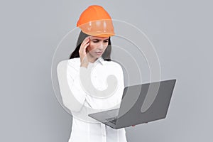 Business builder woman with laptop computer, portrait on gray. Portrait of female worker in hardhat helmet.