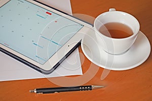 Business, calendars, appointment. Office table with notepad, computer, coffee cup.