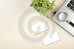 Business card blank, laptop, flower and magnifying glass at office desk table top view. Corporate stationery branding