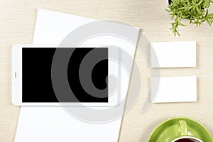 Business card blank, smartphone or tablet pc, flower and coffee cup at office desk table top view. Corporate stationery