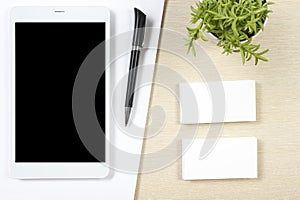 Business card blank, smartphone or tablet pc, flower and pen at office desk table top view. Corporate stationery