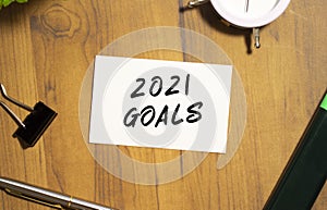A business card with the text 2021 GOALS lies on a wooden office table among office supplies