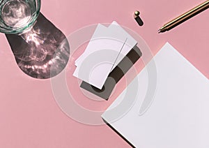Business card white mosk up on the colorful pink background with notepad, pen and glass of water flat lay. Top view.
