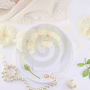 Business cards mockup on a white plate with roses and pearl necklace.