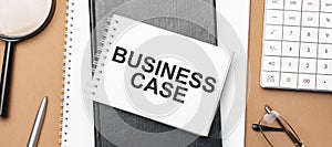 BUSINESS CASE on notepad and various business papers on brown background. Brown glasses and magnifier with notepad