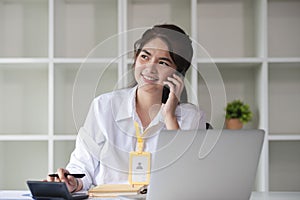 Business Caucasian woman Talking on the phone and using a laptop with a smile while sitting at modern office