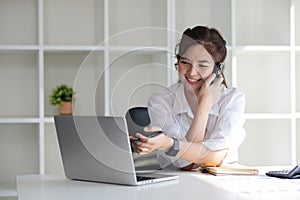 Business Caucasian woman Talking on the phone and using a laptop with a smile while sitting at modern office