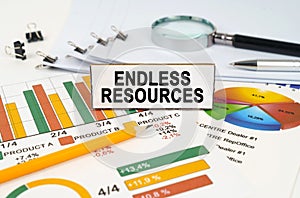 On the business charts lies a magnifying glass, a pen and a sign with the inscription - Endless Resources