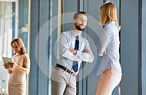 Business colleagues discussing plans while leaning on window in office hall