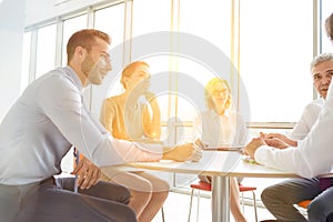 Business colleagues discussing while sitting at table in new office with yellow lens flare in background