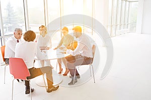 Business colleagues discussing while sitting at table by window in new office with yellow lens flare in background