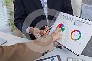 Business colleagues are engaged in a collaborative discussion, analyzing financial charts and reports on the wall and table. They