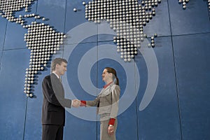 Business colleagues shaking hands in front of world map on office wall