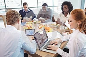 Business colleagues using laptop and digital tablets around breakfast table