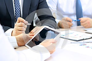 Business colleagues working and analyzing financial graphs on a digital tablet.